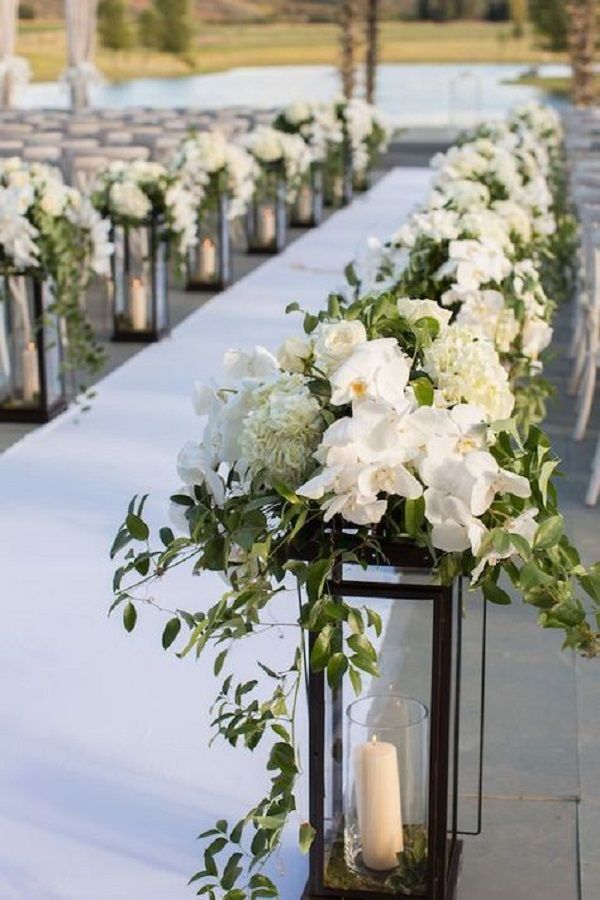 an outdoor ceremony with white flowers and greenery on the aisle, lit by candles