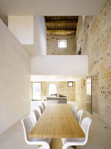 a wooden table surrounded by white chairs in a room with exposed brick walls and ceilings