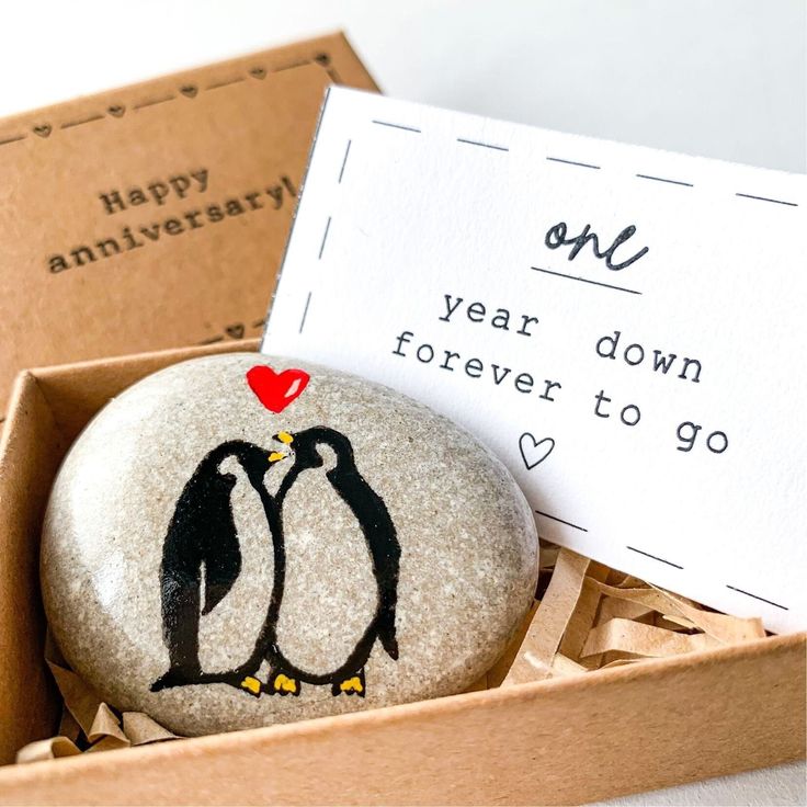 two rocks with penguins painted on them in a box and one has a note that says, one year down forever to go