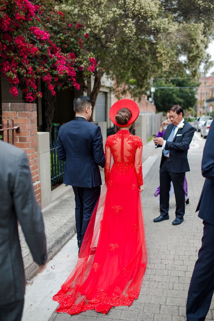 a woman in a red dress is walking down the street with two men wearing suits