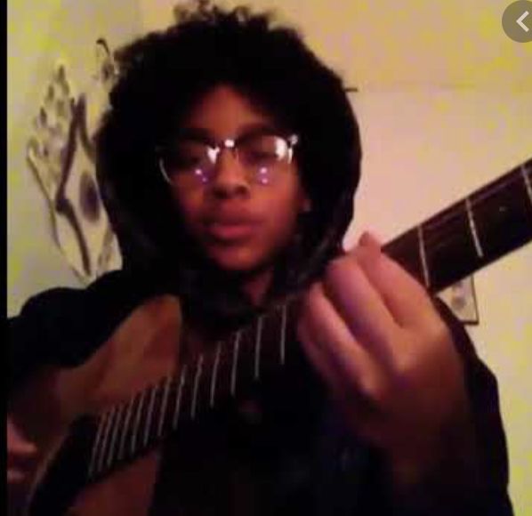 a person with glasses holding a guitar in front of their face and looking at the camera