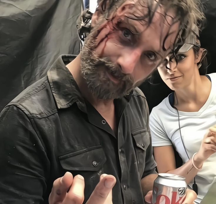 a man with blood all over his face holding a can of ok beer while standing next to a woman