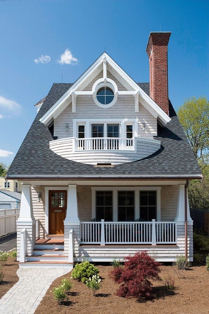 a white two story house with a black roof and front porch on a sunny day