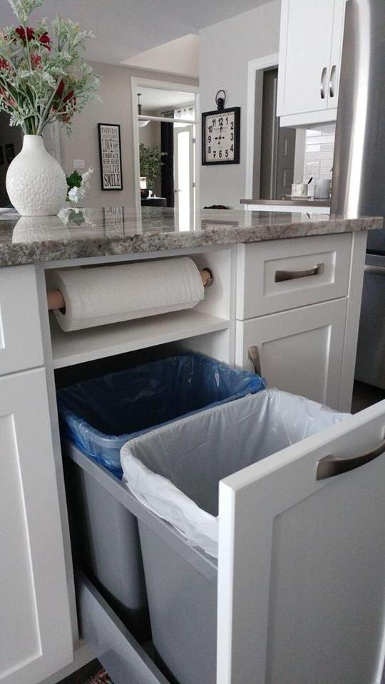 a kitchen with white cabinets and trash cans in the bottom drawer, next to a counter