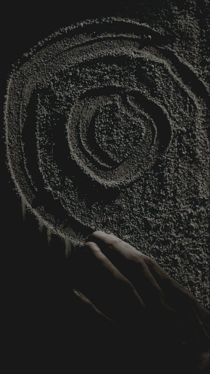 someone is holding their hand in front of a spiral design on the sand that they are drawing