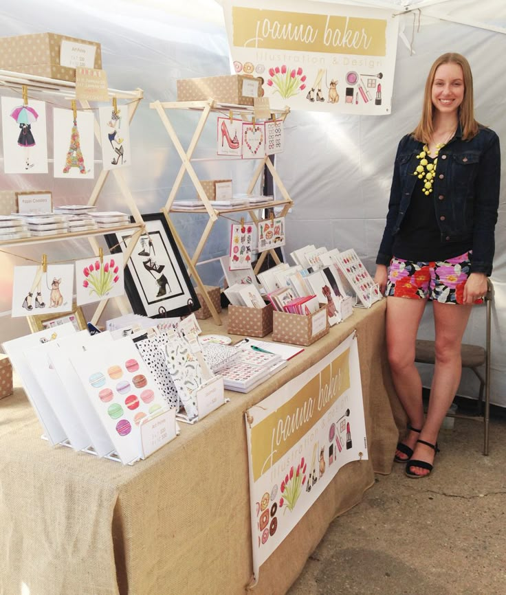 a woman standing next to a table with greeting cards on it at an outdoor market