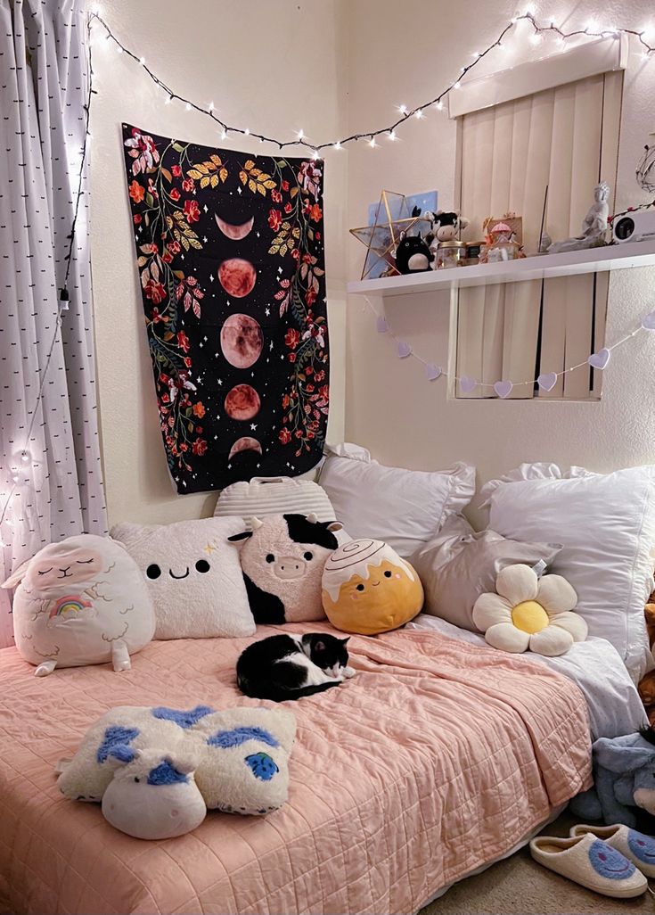 several stuffed animals sit on the bed in this bedroom with lights strung above it and a tapestry hanging over the headboard