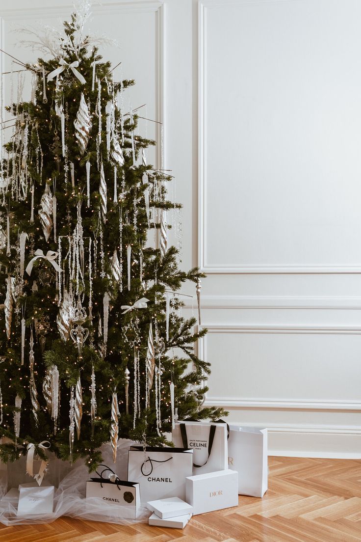 a small christmas tree is decorated with white and silver ribbons, wrapped in gift bags