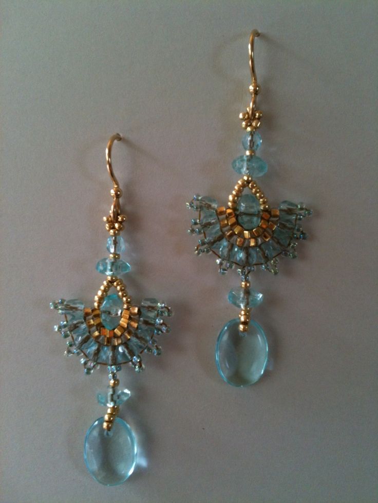 two pairs of blue and gold earrings on a white surface, one is dangling from the ear