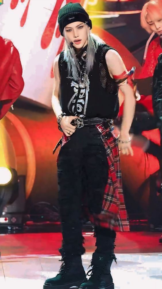 a male in a black shirt and plaid pants is standing on stage with his hands behind his back