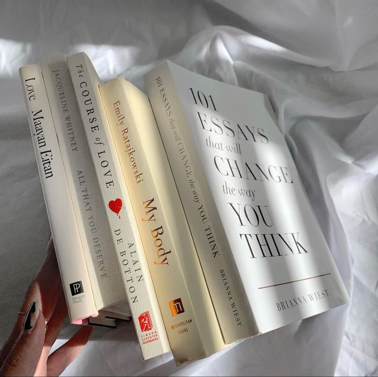 three books sitting on top of each other in front of a white sheet covered bed