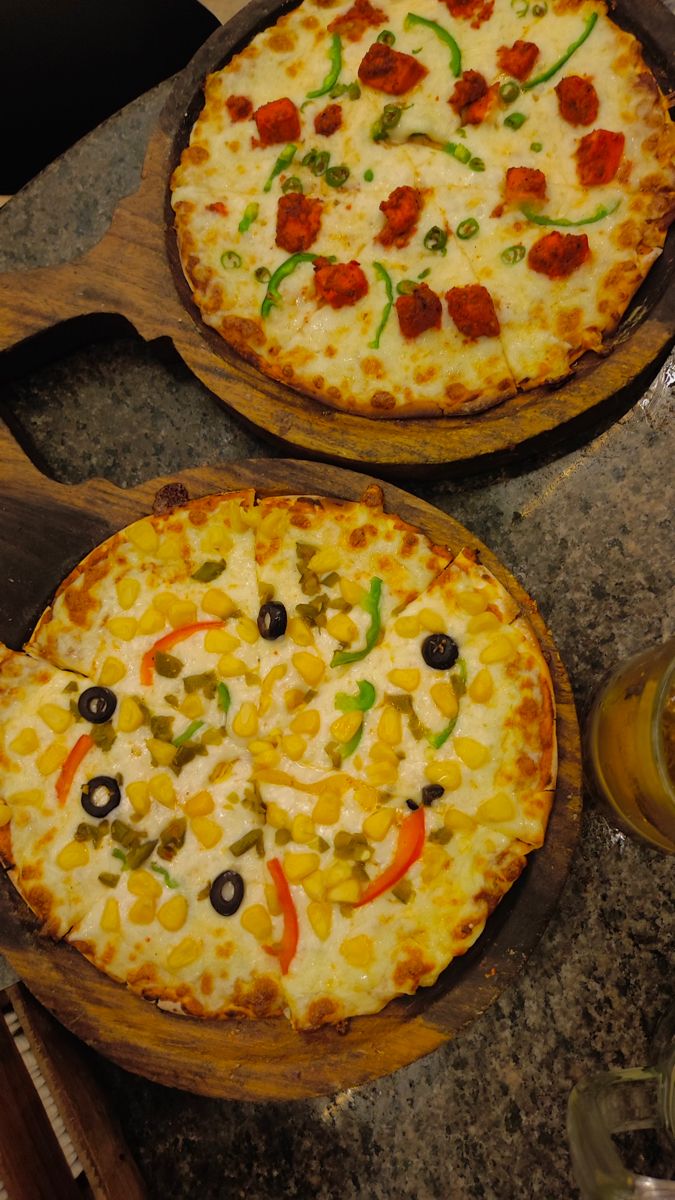 two pizzas sitting on top of wooden pans covered in cheese and toppings