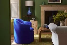 a living room with green walls and blue chairs in front of a fire place that has a painting on the wall