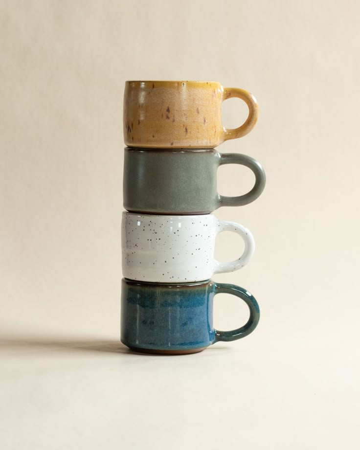 three coffee mugs stacked on top of each other in different colors and shapes,