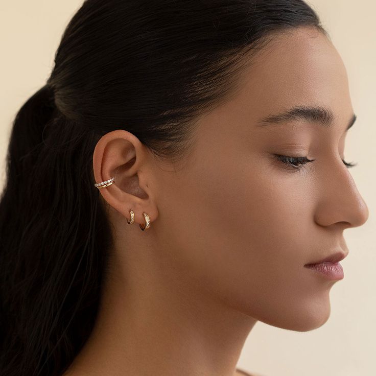 a woman wearing two silver ear rings