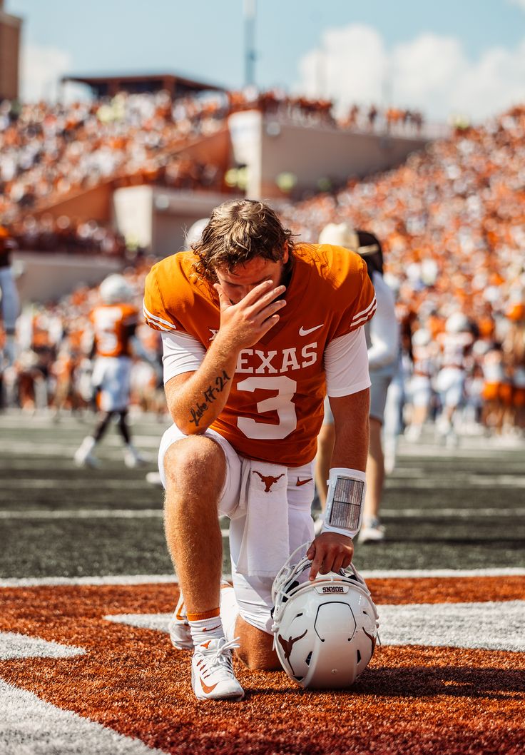 a football player kneeling on the field with his head in his hands and looking down