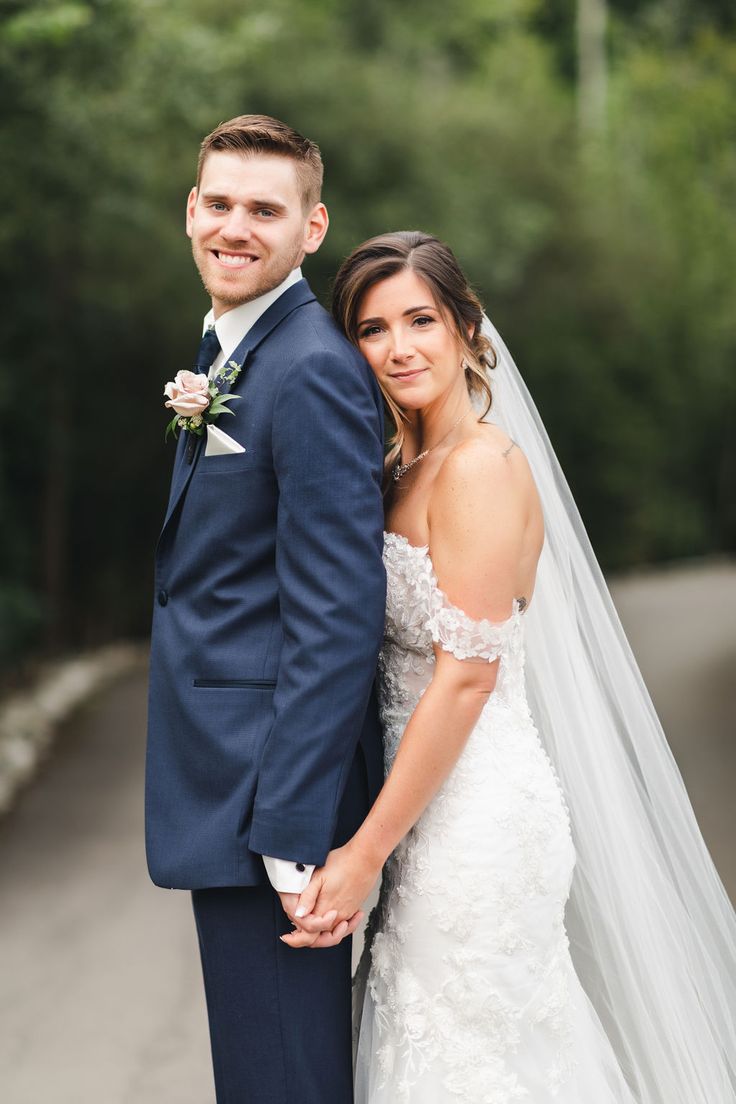 a bride and groom pose for a photo on the street in front of some trees