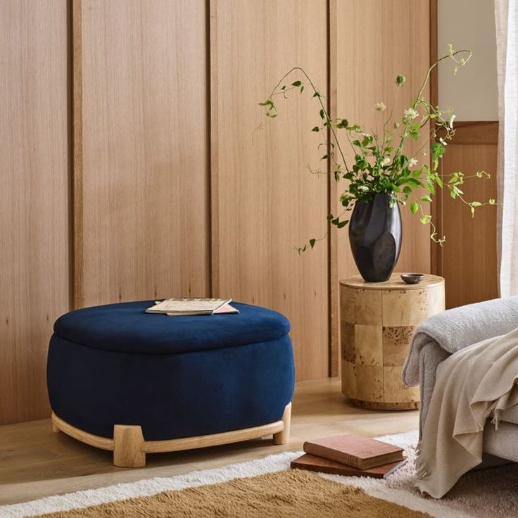 a blue ottoman sitting in front of a bed next to a vase with a plant on it