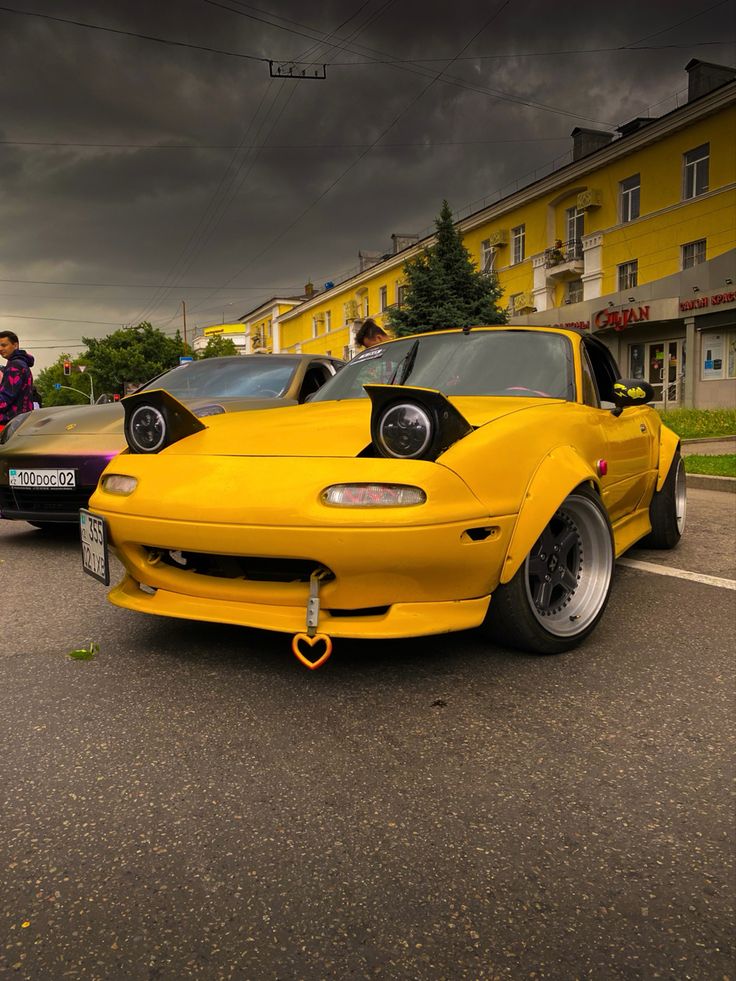 two yellow cars parked next to each other in a parking lot with dark clouds overhead