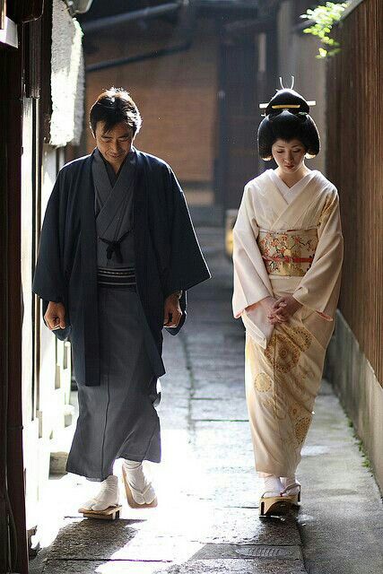 two people dressed in traditional japanese clothing walking down an alley