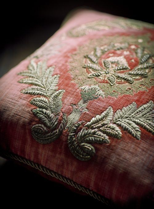 a close up of a red and gold pillow with green leaves on it's side