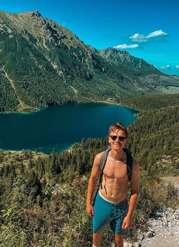 a man standing on top of a mountain next to a lake