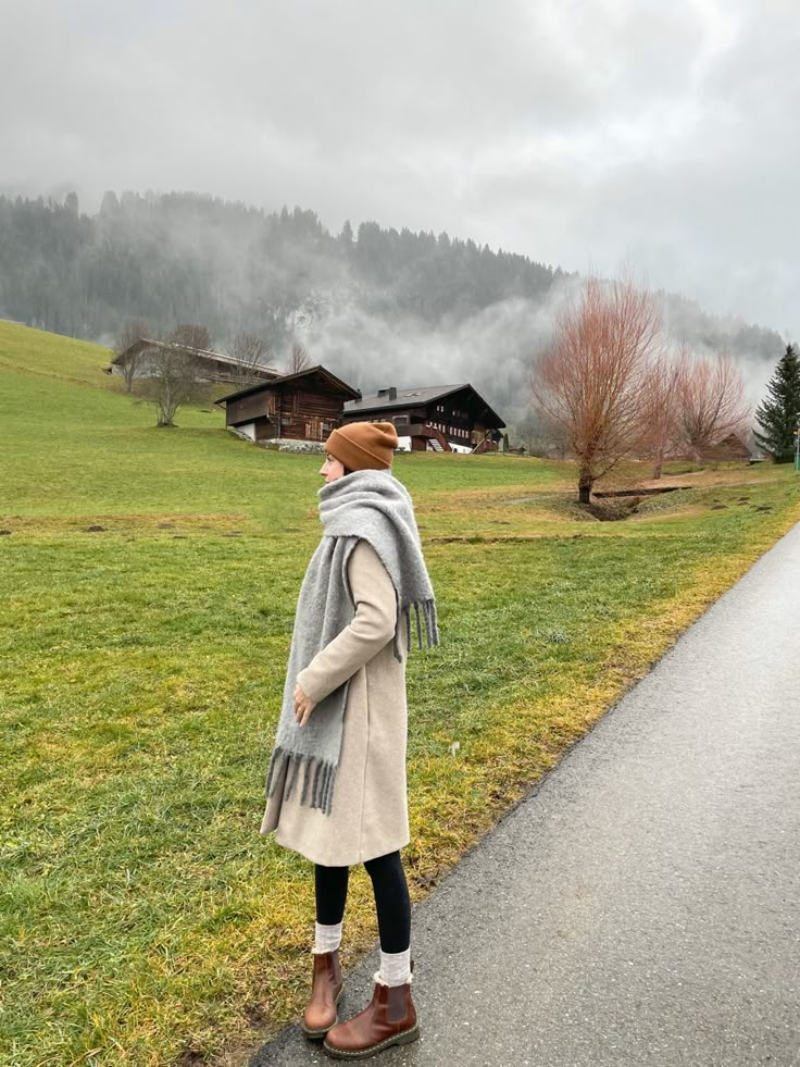 a woman standing on the side of a road with a scarf around her neck and boots