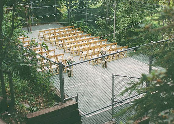 an outdoor tennis court with rows of wooden chairs set up on top of it, surrounded by trees