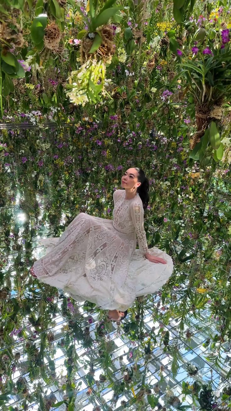 a woman is floating in the air surrounded by plants and flowers with her arms outstretched