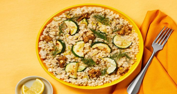 a yellow bowl filled with rice, cucumbers and other vegetables next to a fork