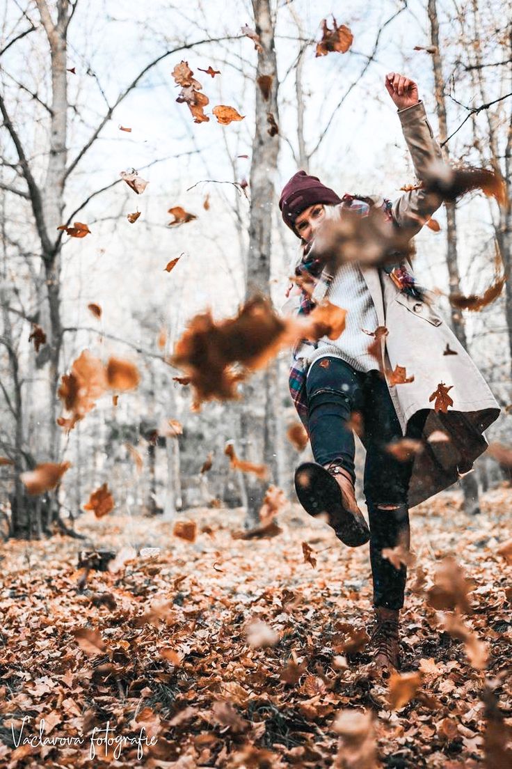 a woman is running through leaves in the woods with her arms up and head down