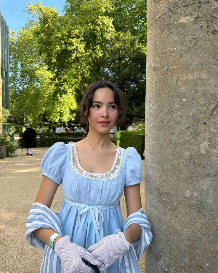 a woman in a blue dress standing next to a pillar