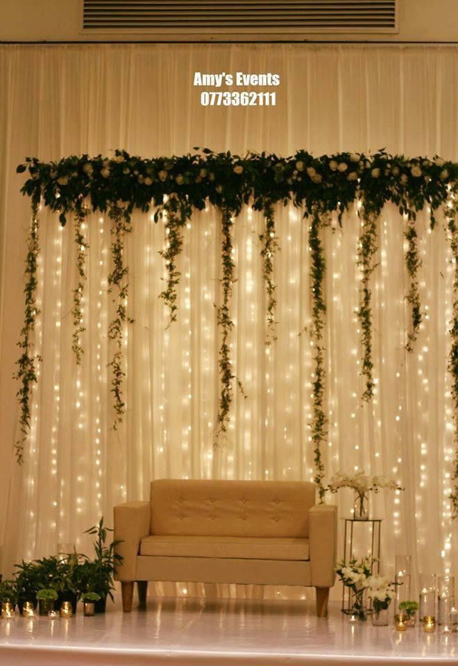 a couch sitting in front of a white curtain covered wall with greenery on it