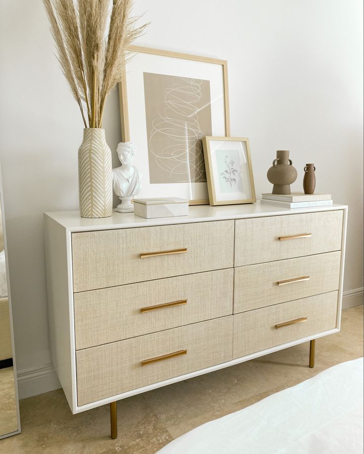 a white dresser topped with lots of drawers next to a vase filled with dried grass