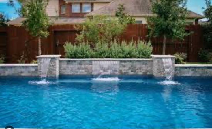 an outdoor swimming pool with water features in the center and side wall, surrounded by greenery