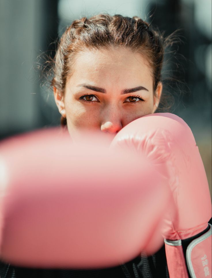 a close up of a woman wearing boxing gloves and looking at the camera with an intense look on her face