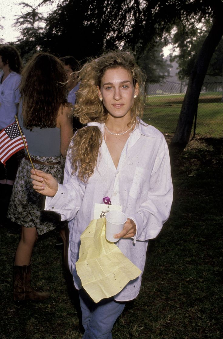 a young woman holding a cup and an american flag in her hand while walking through a park