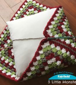 a crocheted blanket is laying on the floor next to a pillow and knitting needles