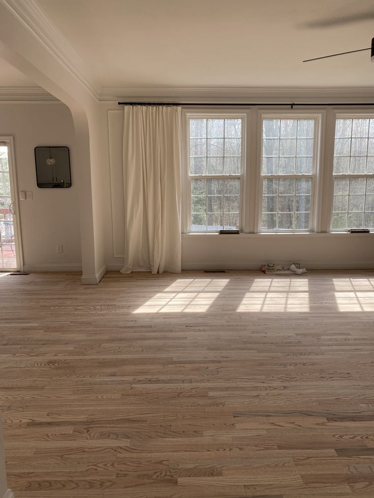 an empty living room with hard wood floors and white curtains on the window sill