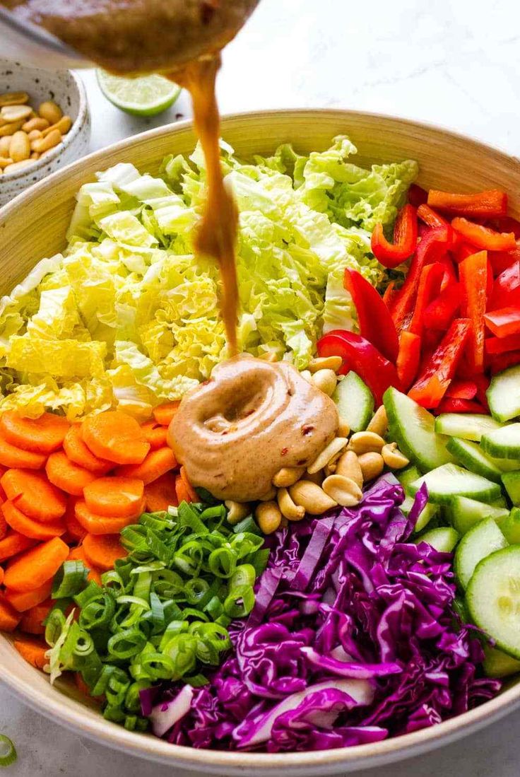 a bowl filled with vegetables and dressing being drizzled over the salad ingredients