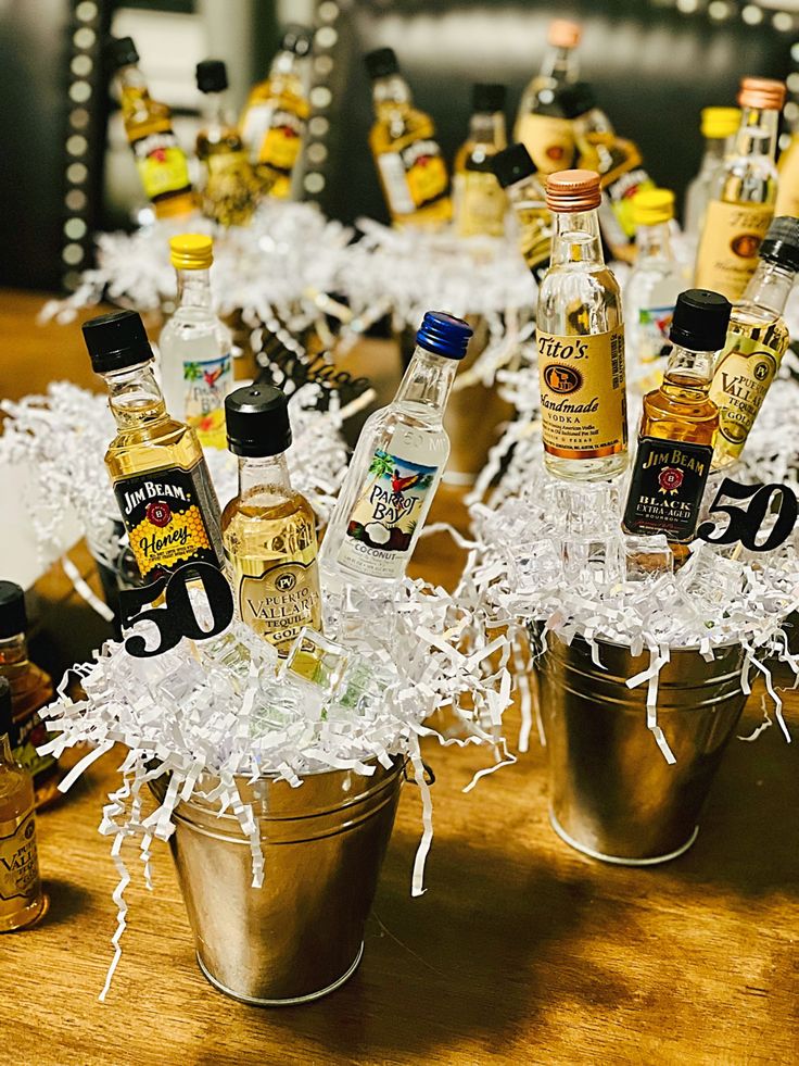 several bottles of alcohol are sitting in small buckets on a table with shredded white paper