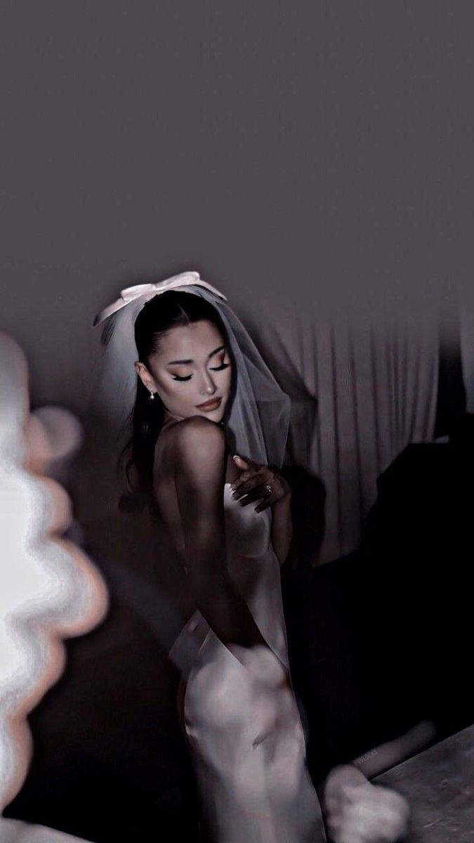 a woman in a white wedding dress is holding her veil over her head and looking down at the floor