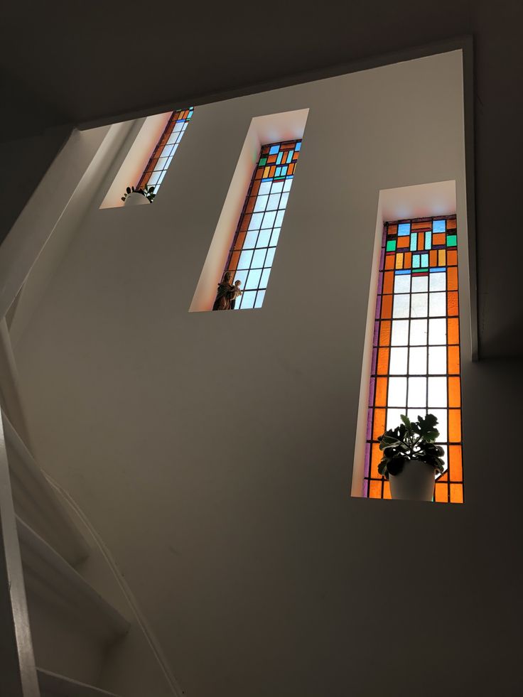 three colorful stained glass windows on the side of a white wall and stair casement