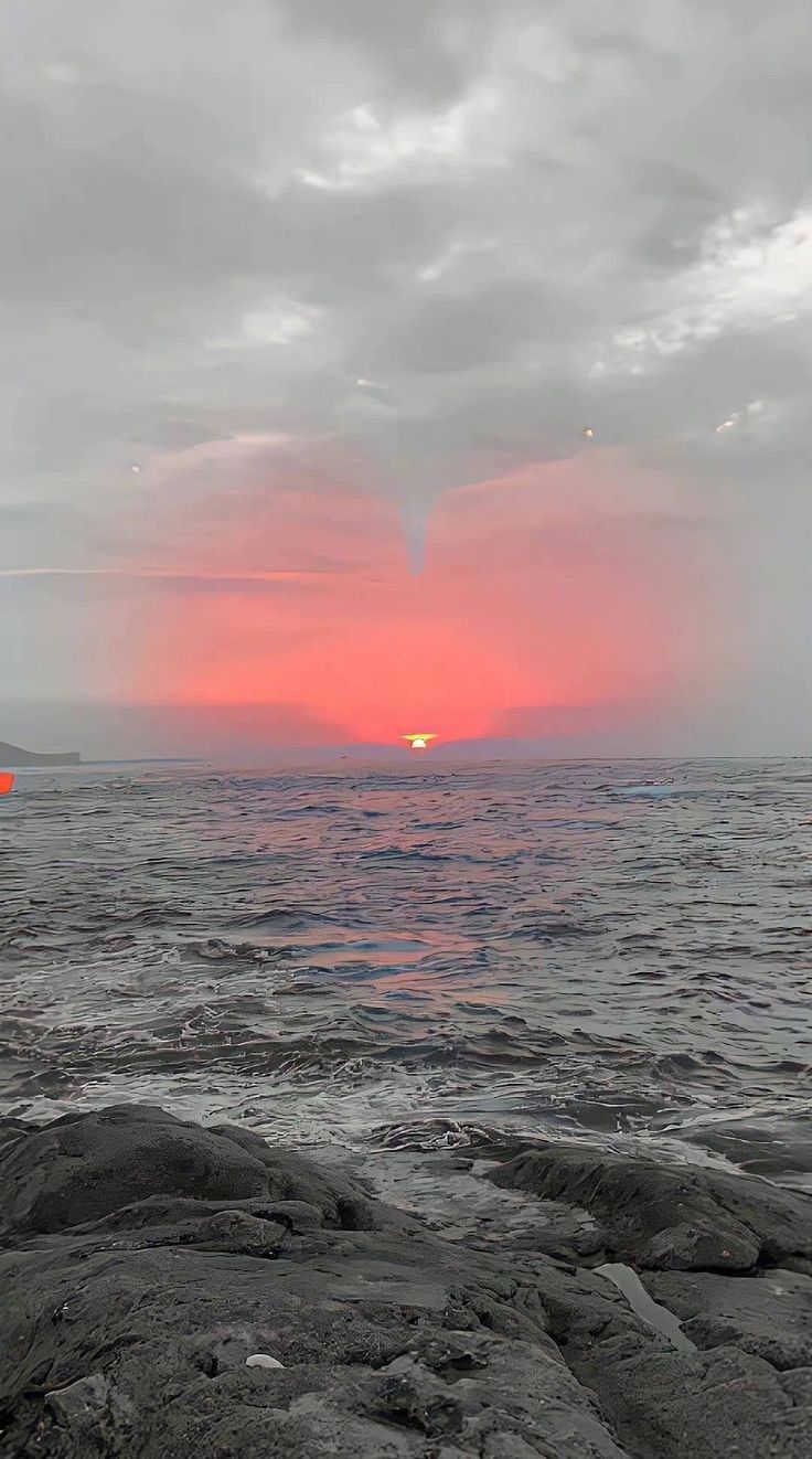 the sun is setting over the ocean with rocks