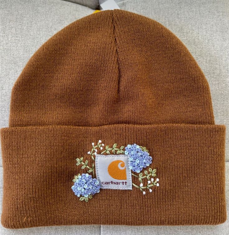 a brown beanie with blue flowers on the front and white patch in the middle