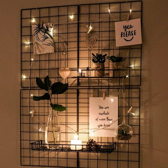 a metal wire wall hanging with plants and lights on it, next to a sign that says we please