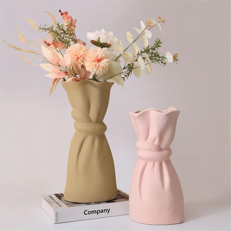 two vases with flowers in them sitting next to each other on top of a book