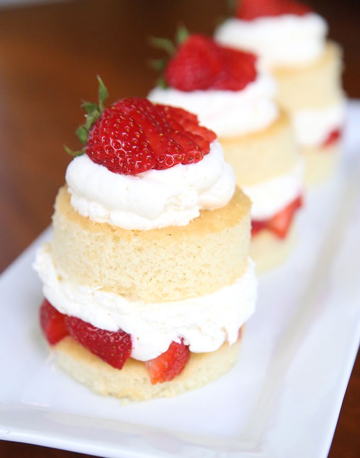 three small cakes with whipped cream and strawberries on top are sitting on a white plate