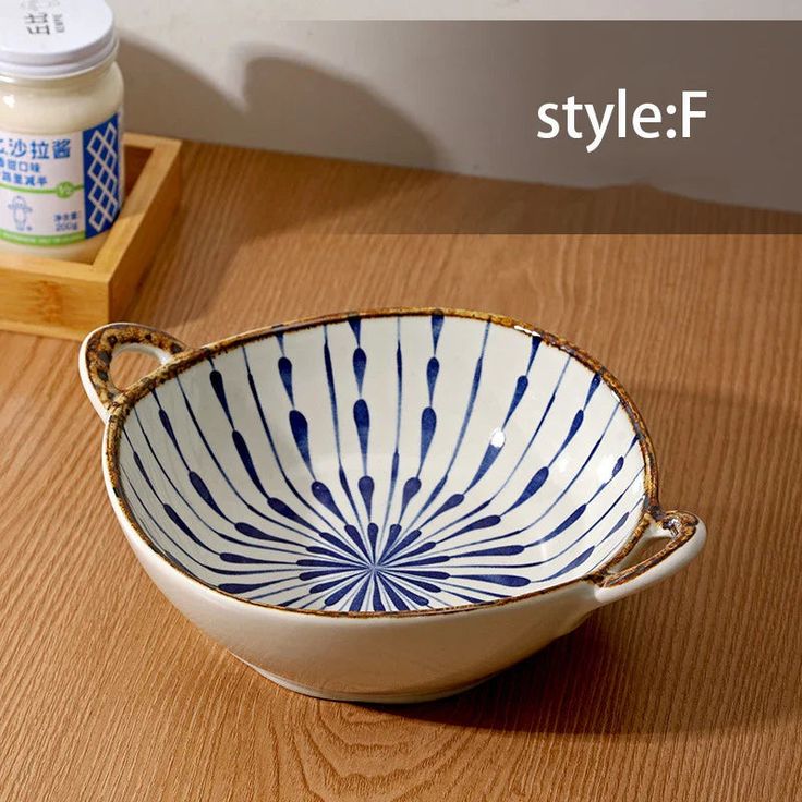 a white and blue bowl sitting on top of a wooden table next to a jar