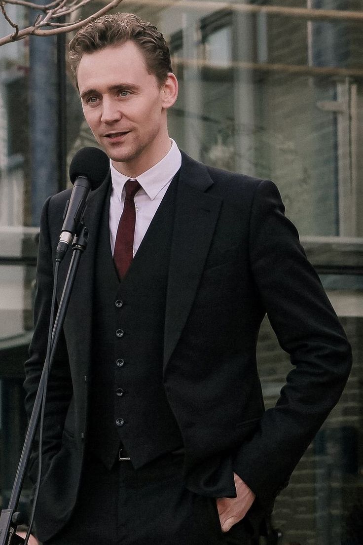 a man wearing a suit and tie standing in front of a microphone with his hands on his hips